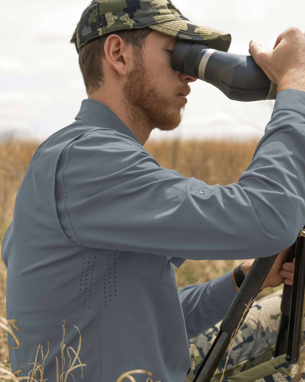 Hunter looking through a spotting scope, wearing the Mesa Vented Long Sleeve Snap Shirt in Slate Blueish Grey