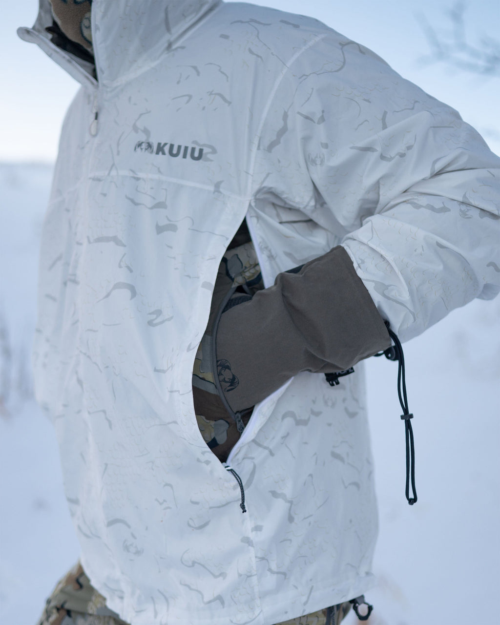 Hunter wearing Snowfall Overwhite Jacket displaying pass-through zipper openings for access to under layer pockets