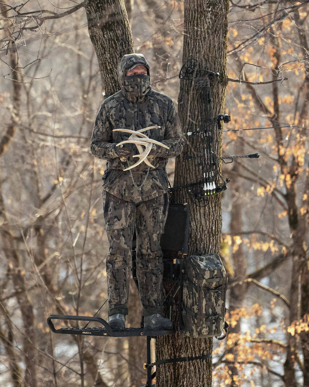 Hunter standing in a treestand rattles two deer antlers together wearing StrongFleece 290 Gloves in Veros Camouflage.