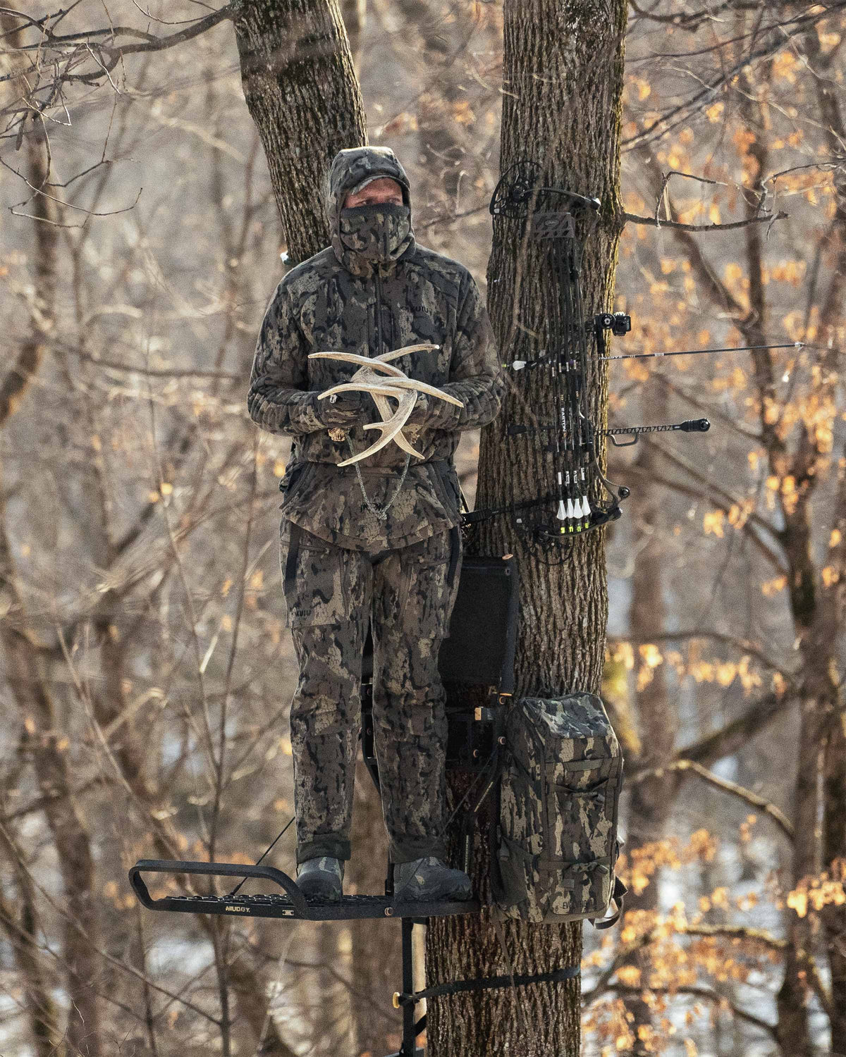 Hunter standing in a treestand rattles two deer antlers together wearing StrongFleece 290 Gloves in Veros Camouflage.