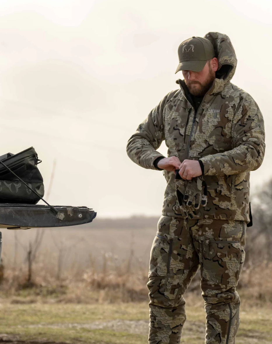 Hunter suited in KUIU Proximity Insulated Pant and Proximity Hooded Insulated Jacket putting on Axis Glove in Valo Camouflage