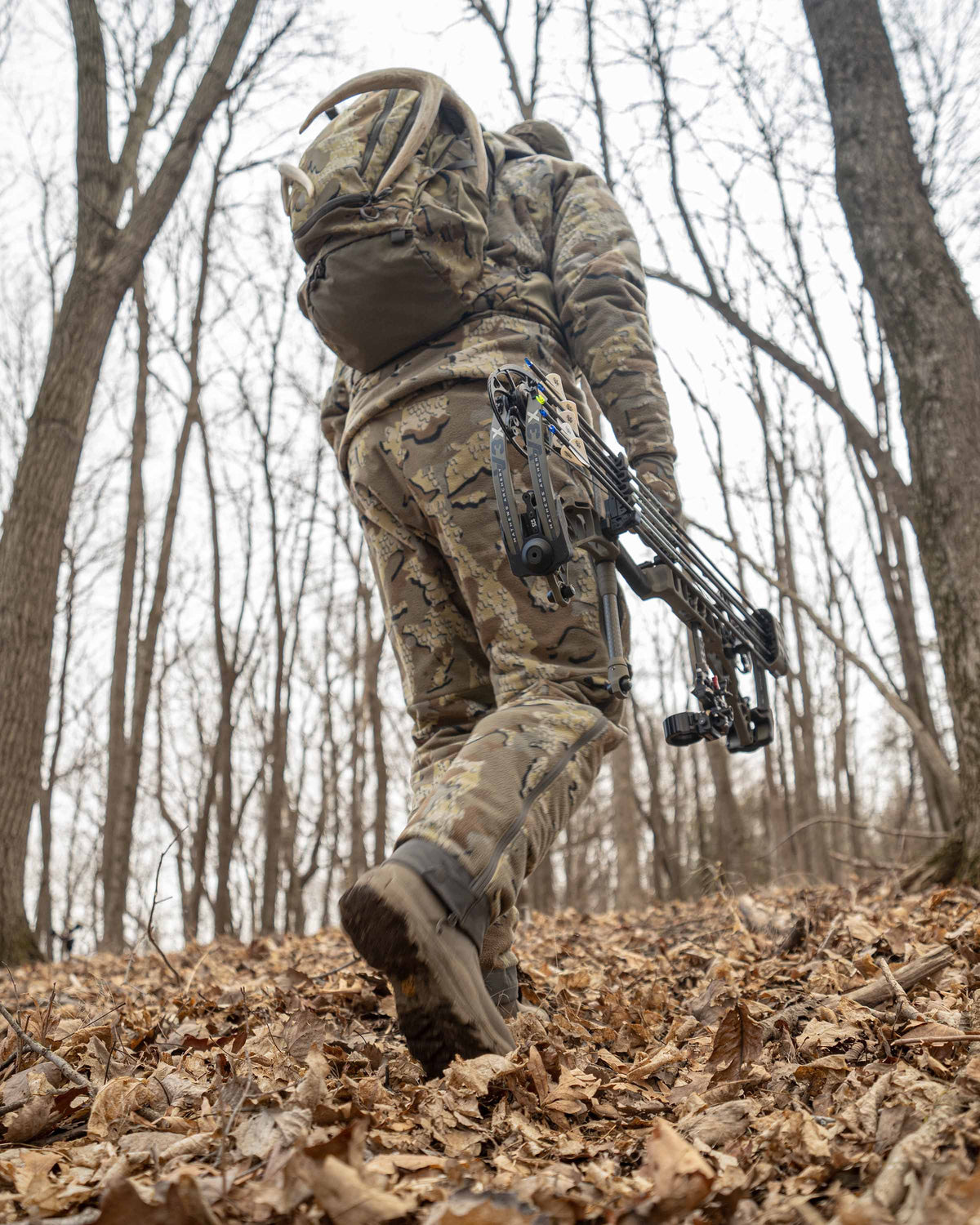 Rear, Angled View of Hunter Carrying Bow in Hardwoods Wearing Proximity Insulated Pants in Valo Off-Shade Camouflage