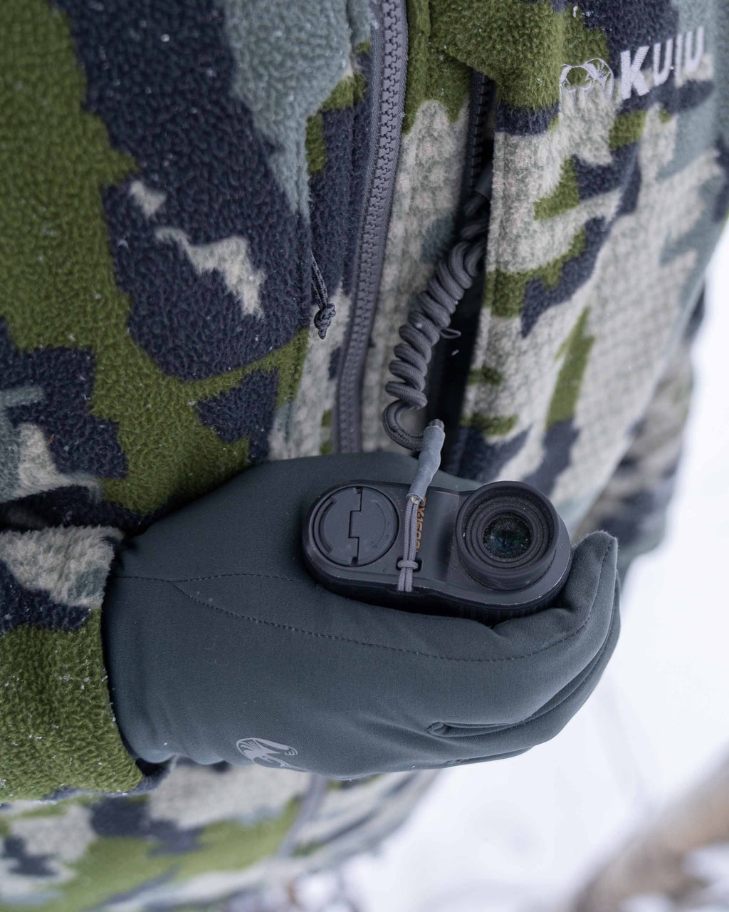 Front of Hunter in Treestand Wearing Proximity Hooded Insulated Jacket in Verde Camouflage Highlighting YKK Zippered Chest Pocket with Interal Accessory Attachment Point (Lanyard Sold Separately)