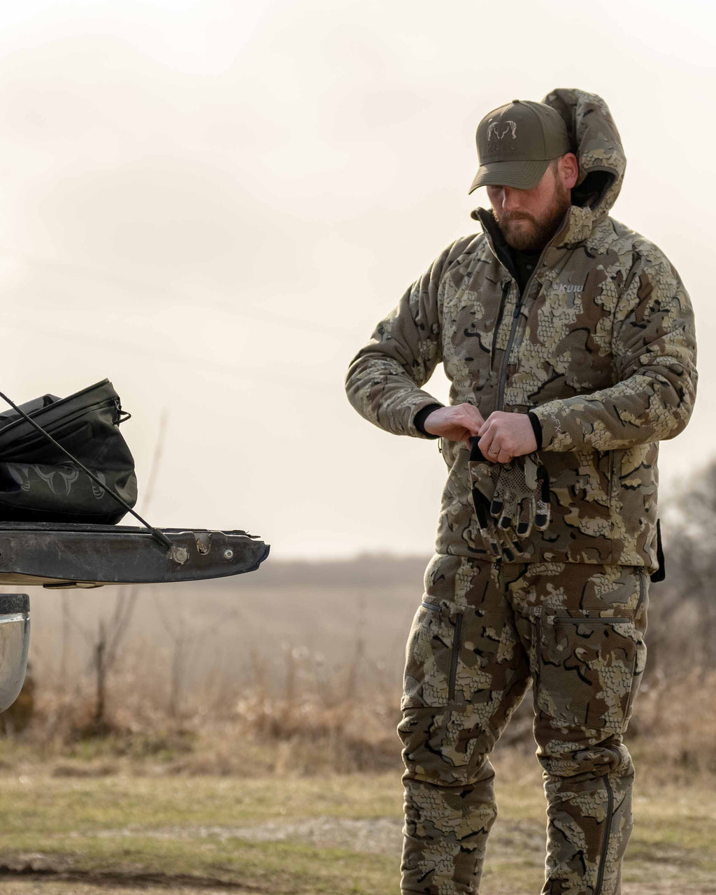 Front, Angled View of Hunter Putting on Gloves Wearing Proximity Hooded Insulated Jacket in Valo Camouflage