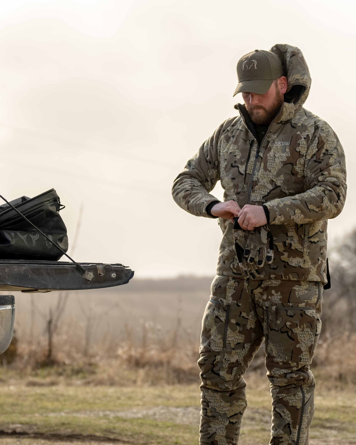 Front, Angled View of Hunter Putting on Gloves Wearing Proximity Hooded Insulated Jacket in Valo Camouflage