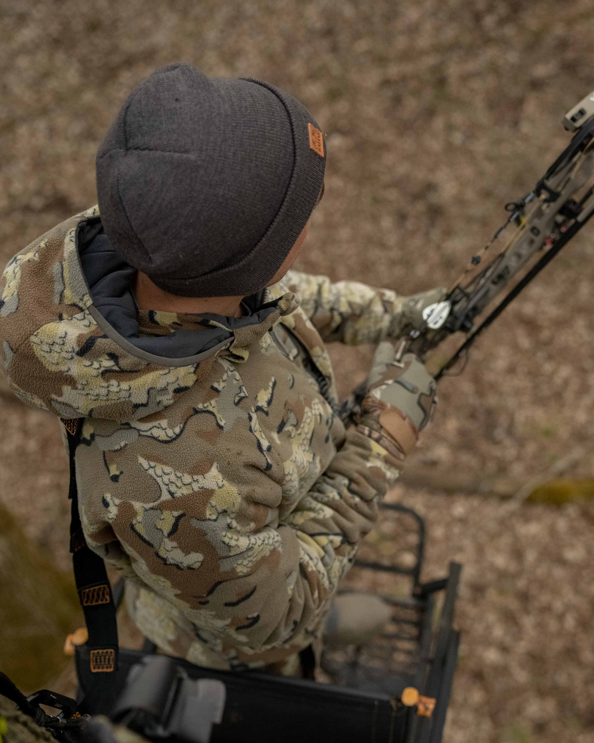 Rear, Aerial View of Hunter in Treestand Wearing Proximity Hooded Insulated Jacket in Valo Camouflage Ready to Draw Bow
