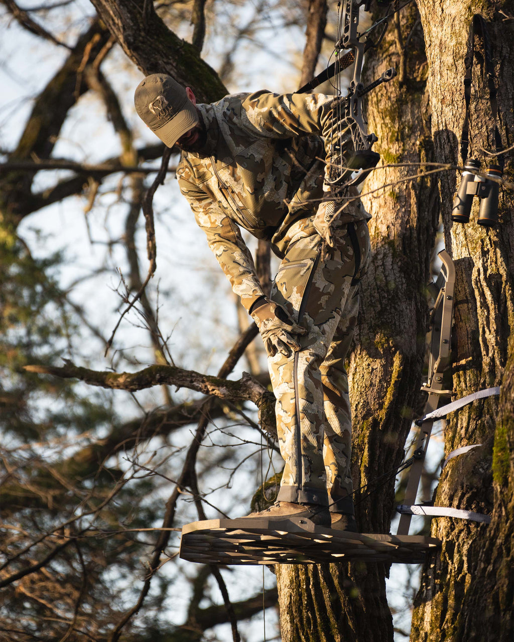 Hunter in treestand wearing Encounter Pant in Valo Camouflage adjusting zippered mesh-lined hip vents for ventilation