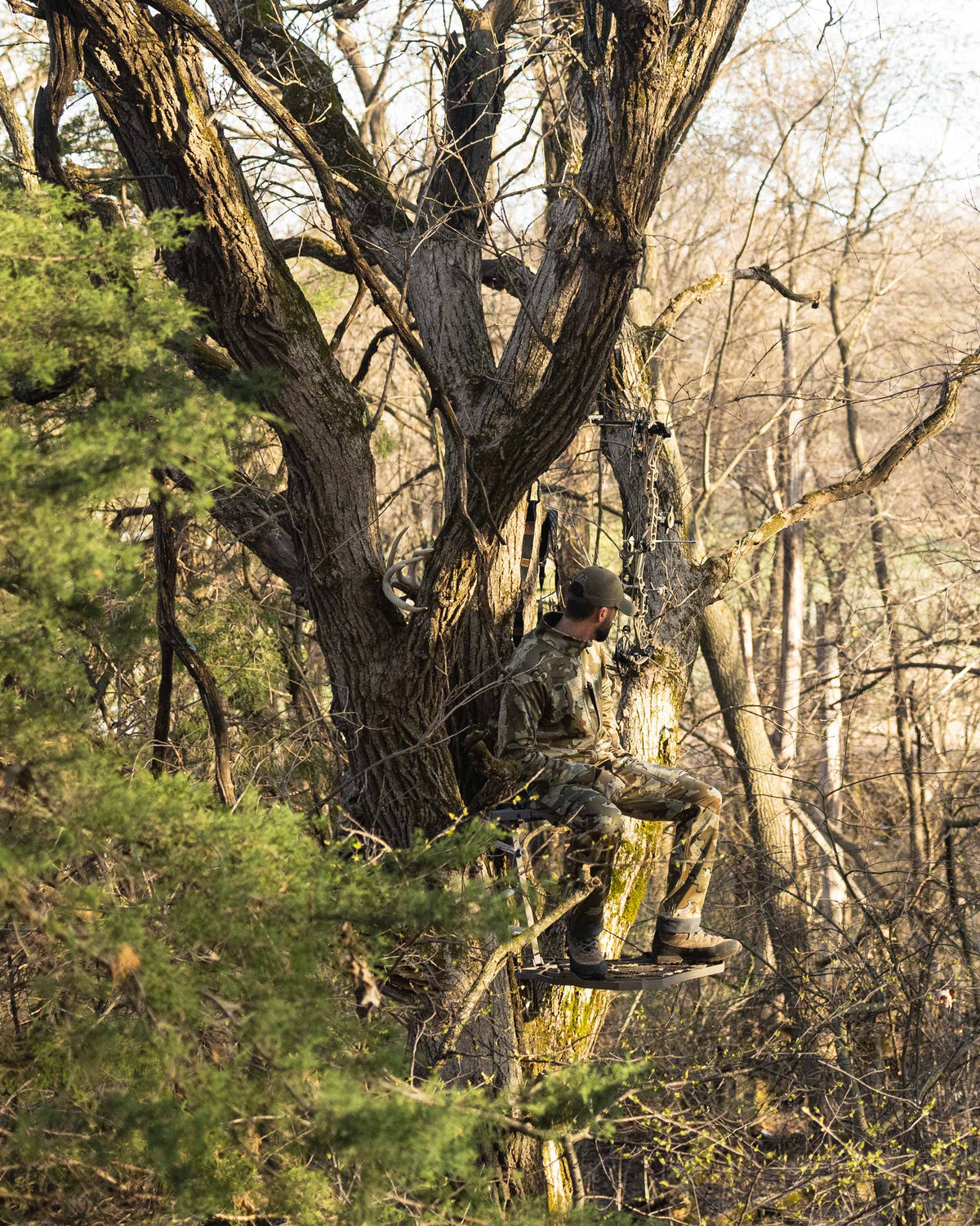 Side profile zoomed out hunter in treestand sitting wearing Encounter Jacket in Valo Camouflage