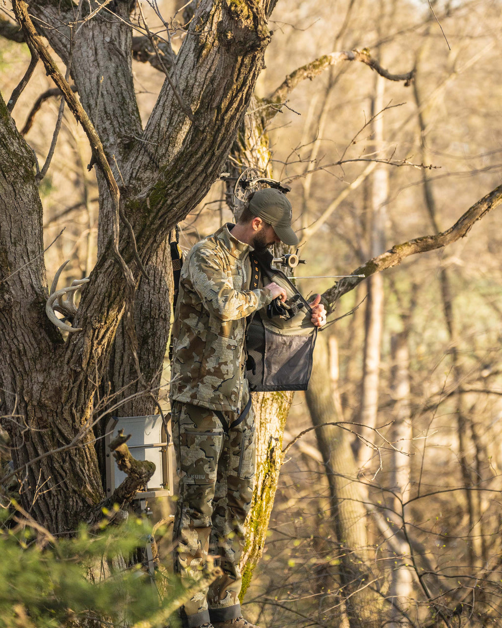Hunter in treestand wearing Encounter Jacket in Valo Camouflage using interior drop pocket to stow gloves