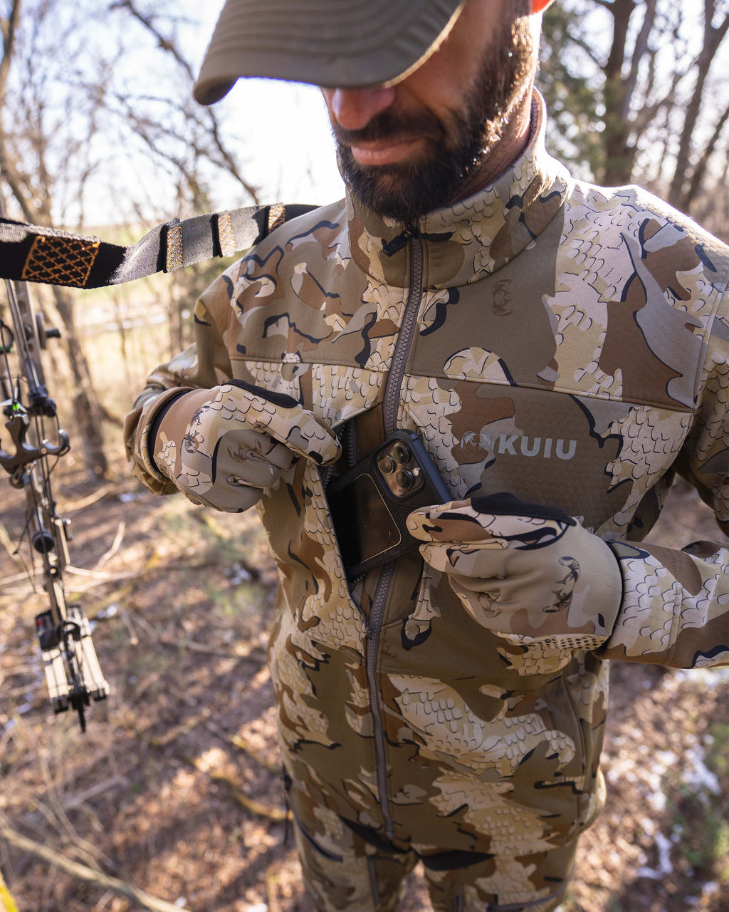 Detail hunter wearing Encounter Jacket in Valo Camouflage placing phone in one of the dual chest pockets