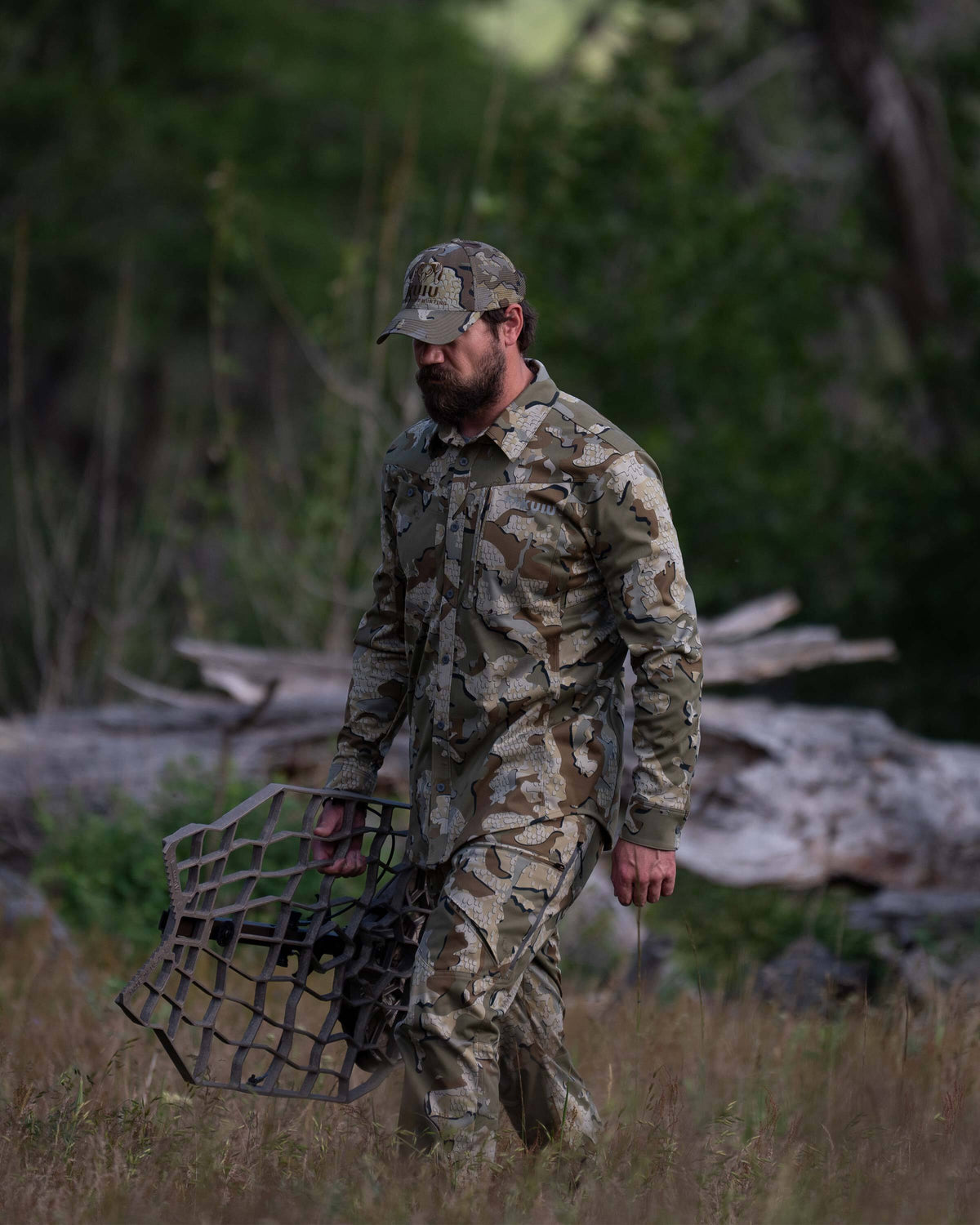 Hunter walking through the meadow, carrying an aluminum treestand, wearing Encounter LT Pant in Valo Camouflage