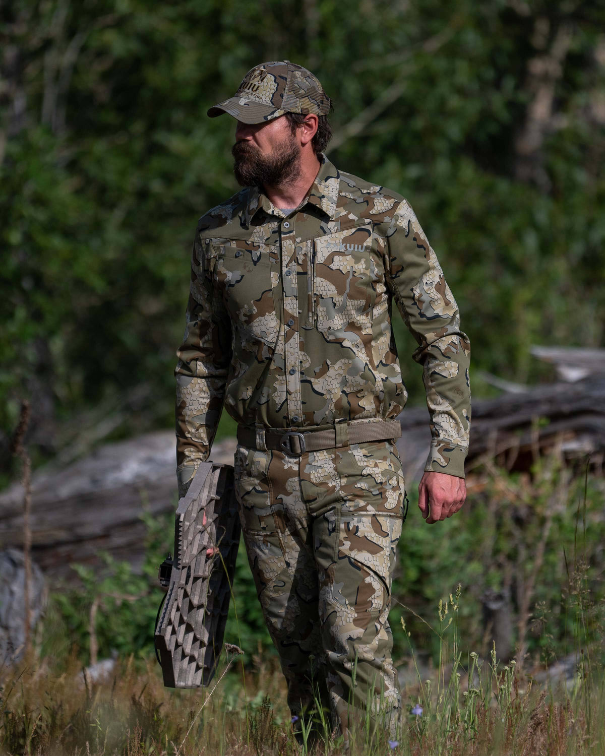Hunter in a meadow setting looking afar, carrying an aluminum treestand, wearing Encounter LT Pant in Valo Camouflage