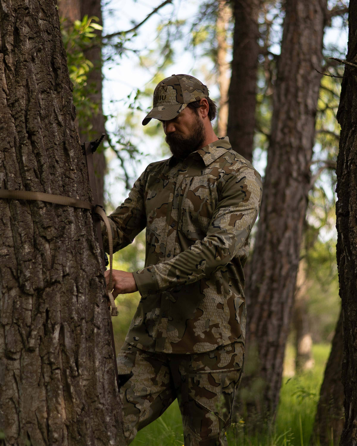 Hunter in a wood setting, focused on adjusting his climbing gear, wearing Encounter LT Shirt in Valo Camouflage