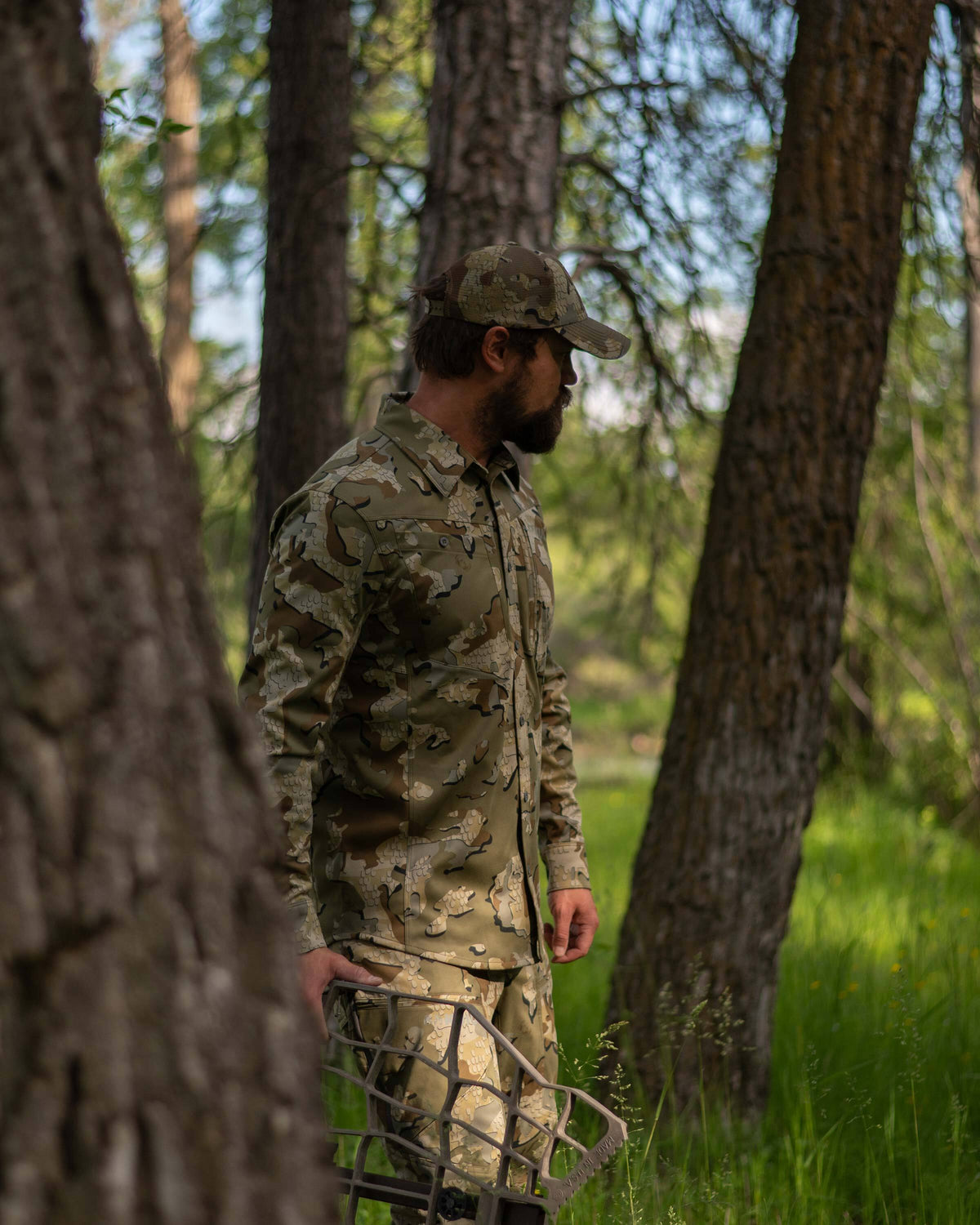 Hunter scouting and walking through the woods carrying an aluminum treestand, wearing Encounter LT Shirt in Valo Camouflage