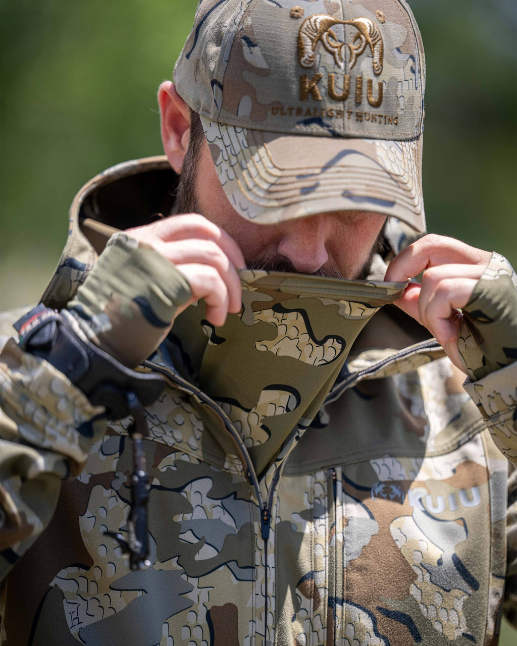 A man wearing a Drawpoint Hoodie in Valo camouflage shown pulling the built-in face covering over his mouth.