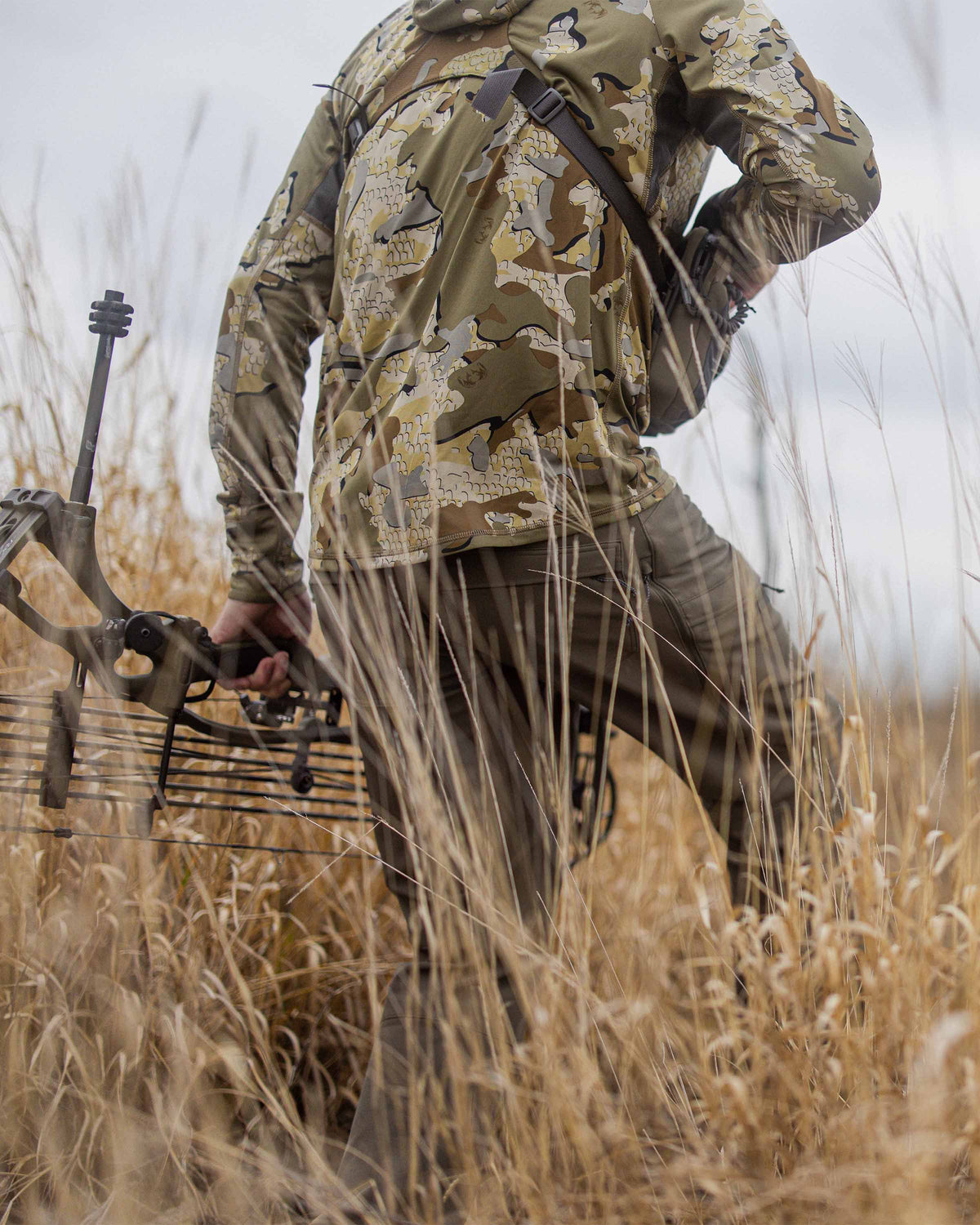Rear, Angled View of Kevin Wilkey Holding Bow Wearing Attack Pants in Ash Brown Color