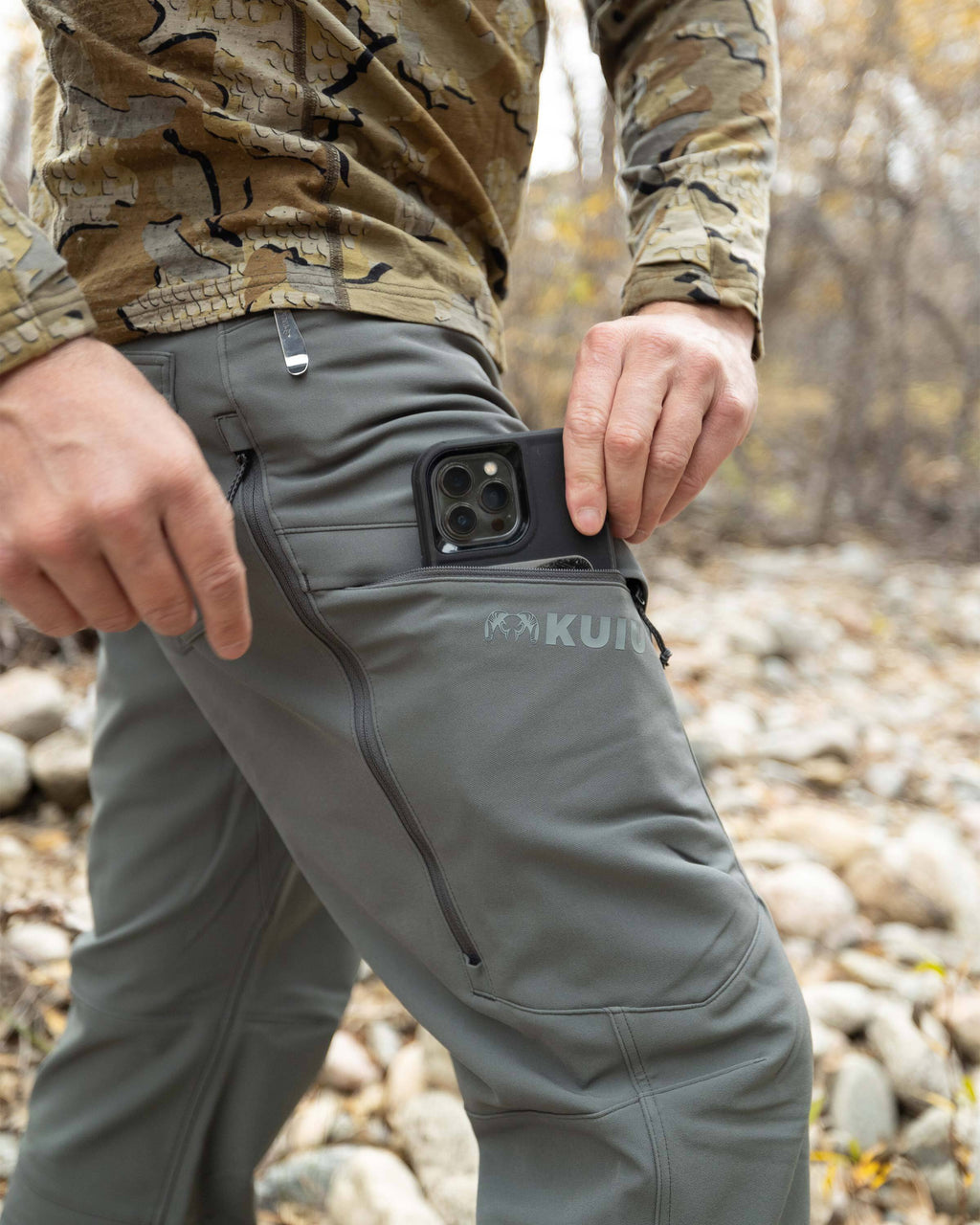 Close-up of Hunter putting a cell phone in the front cargo pocket of the Attack Pant in Stone Grey