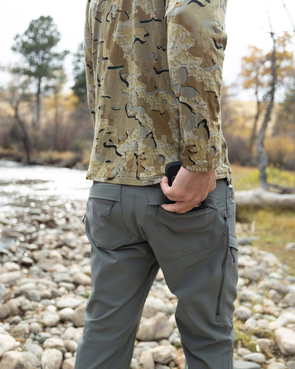 Back view of Hunter putting a cell phone in his right back pocket on the Attack Pant in Stone Grey