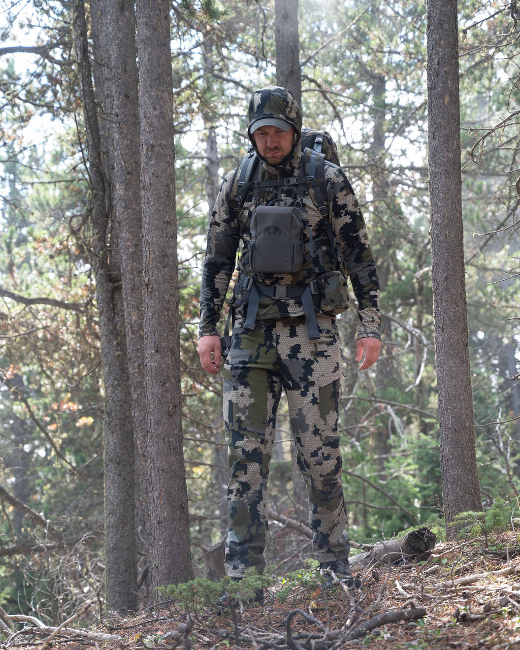 Front of Hunter Hiking in Green Forest Wearing Attack Pants in Verde Camouflage