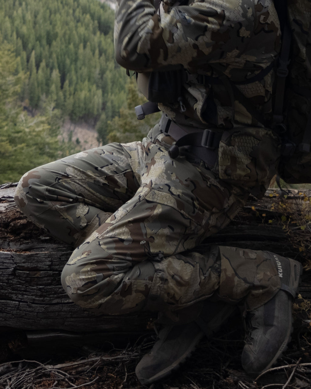 Side of Hunter Sitting on Fallen Tree Wearing Attack Pants in Valo Camouflage Highlighting Articulated Knees
