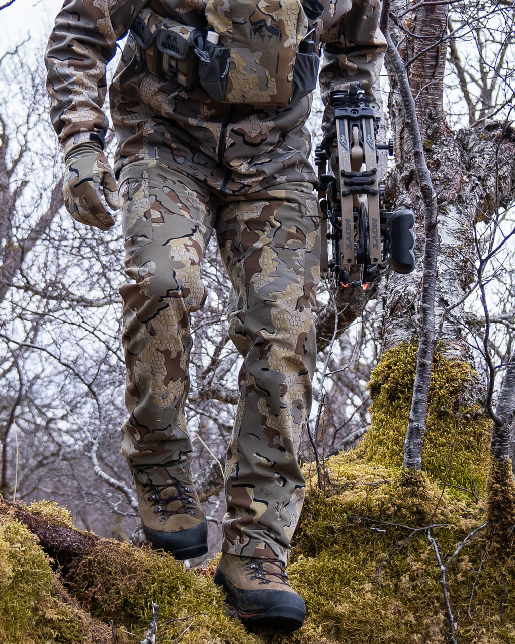 Front of Hunter Hiking Over Moss Covered Log Wearing Attack Pants in Valo Camouflage