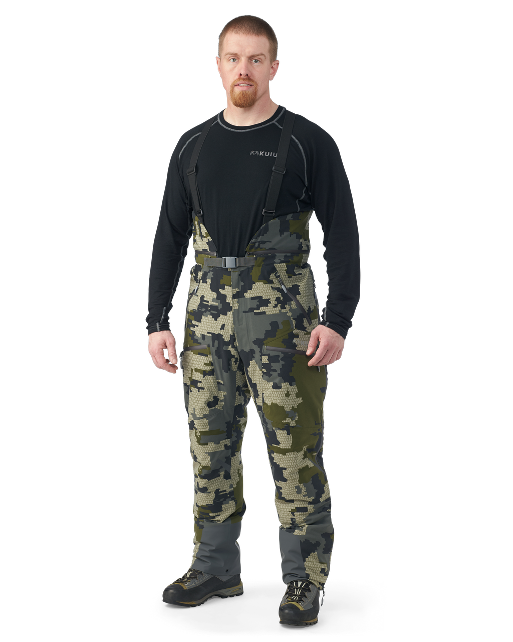 Hunter wearing Kutana Gale Force Pant in Verde Camouflage with suspenders over shoulders
