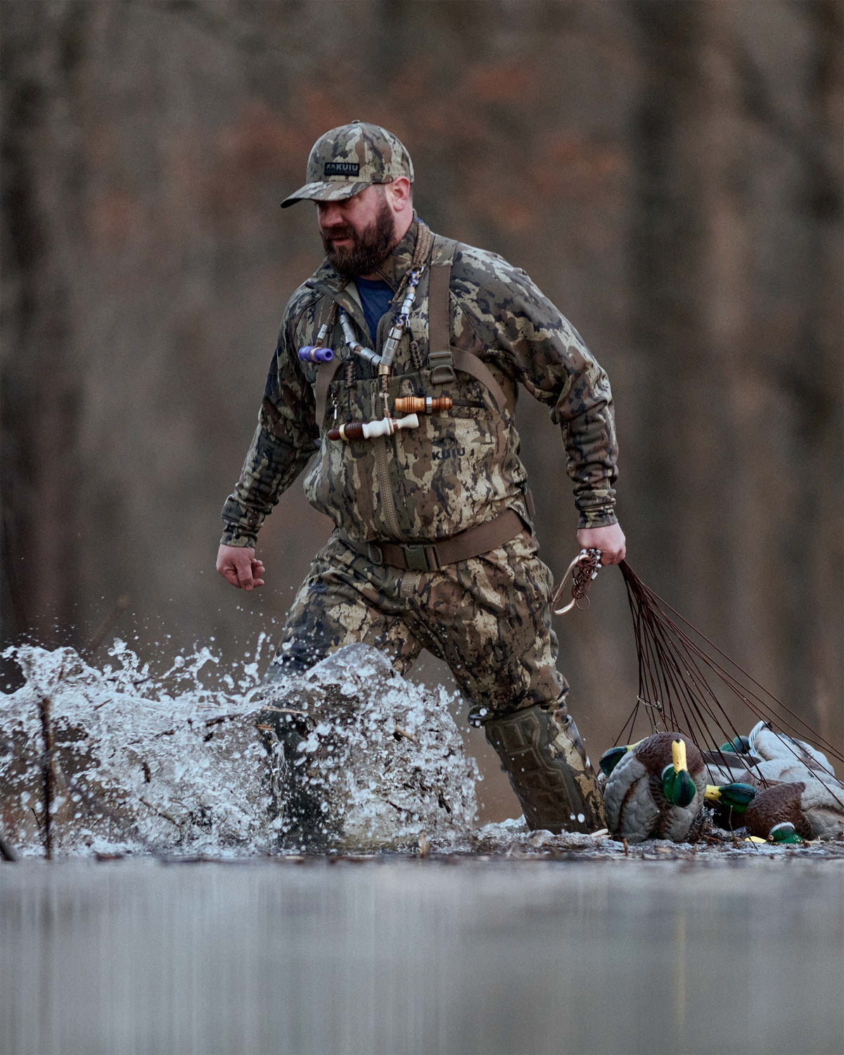 Waterfowl hunter wearing KUIU PRO HD Flex Zip Wader wades through shallow water, pulling a cluster of duck decoys across shallow water.