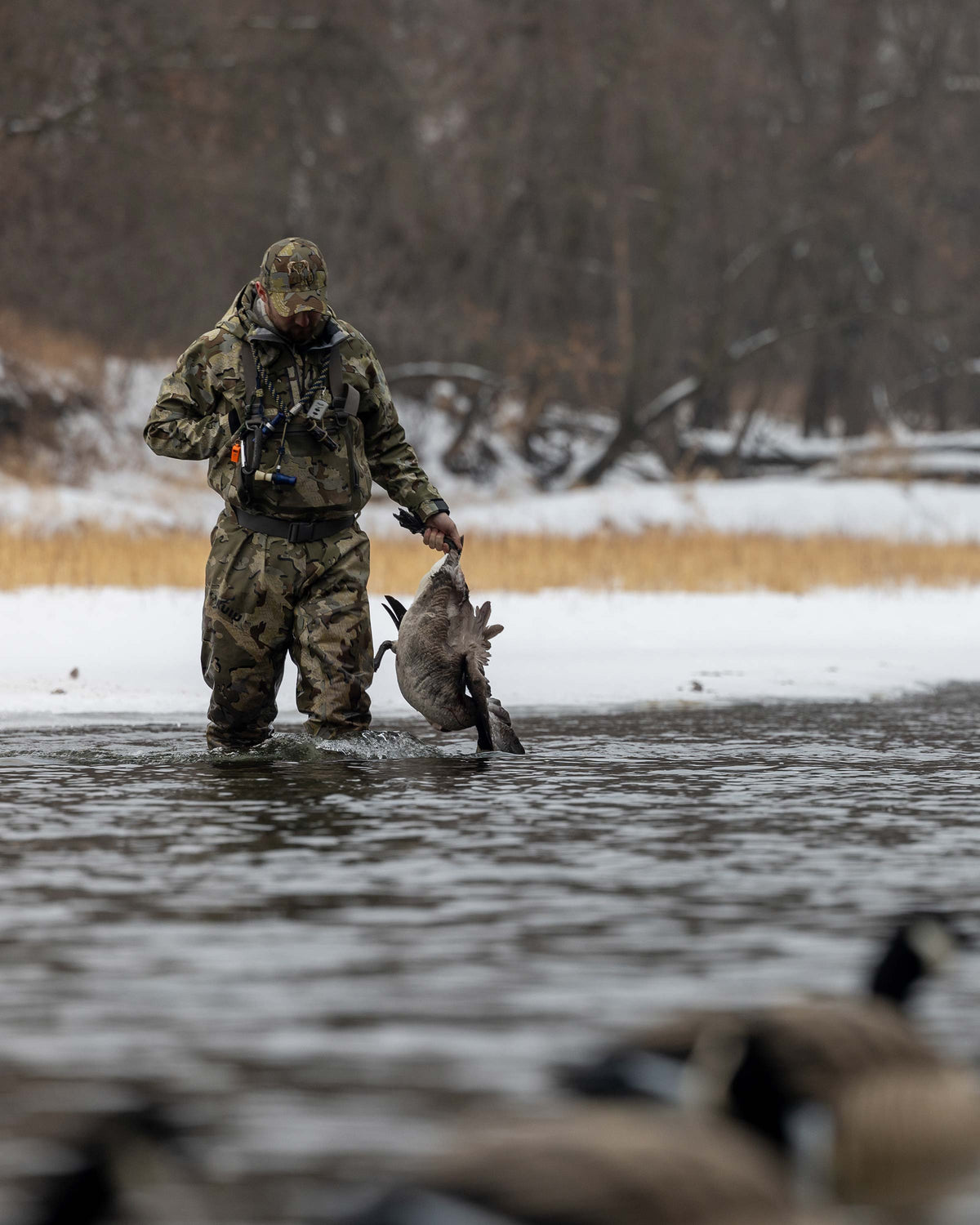 Hunter Wearing HD Flex Waders in Valo Camouflage holding a Canada Goose with ice and snow in the background