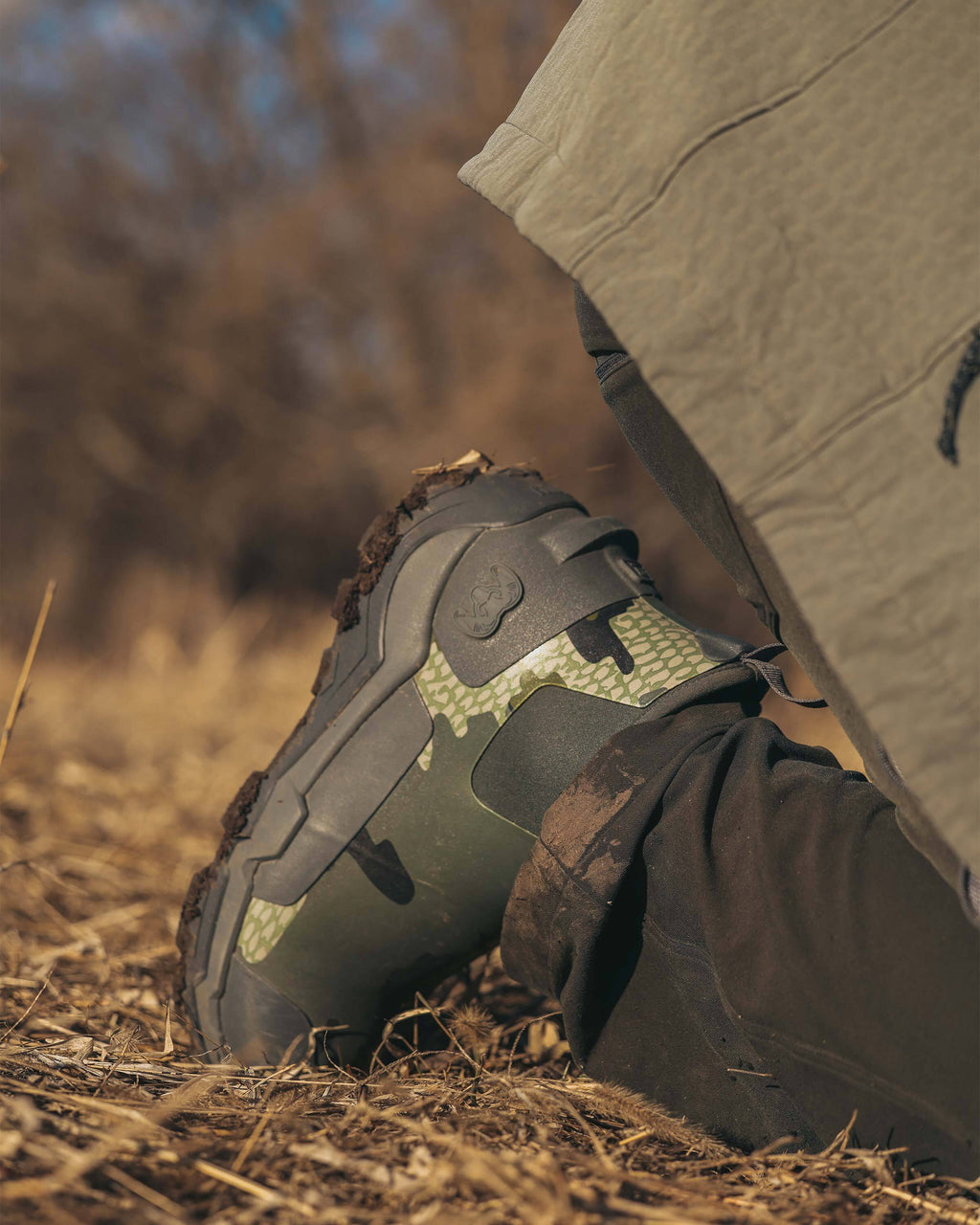 Close-up partial view of hunter kneeling down, Highlight mud on the bottom tread of his KUIU Ankle Mud Boot in Verde Camouflage