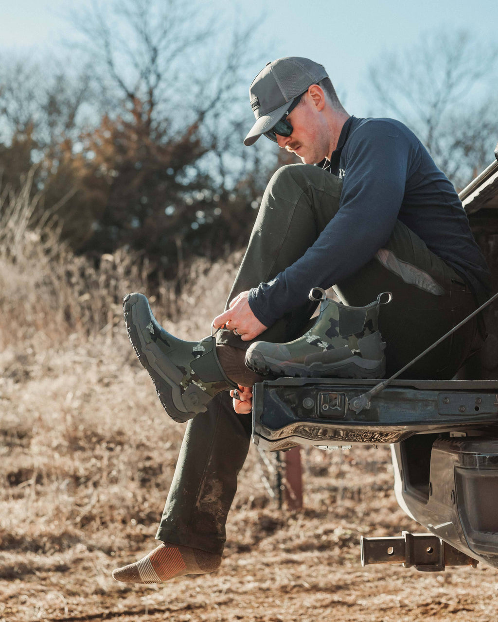 Hunter putting on the KUI Ankle Mud Boot in Verde Camouflage, using front pull-loops 