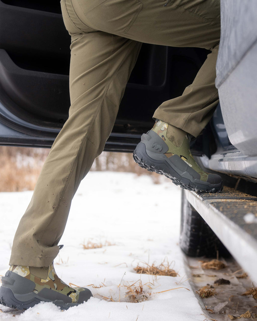 Hunter wearing the KUIU Ankle Mud Boot in Valo Camouflage, stepping up into his vehicle