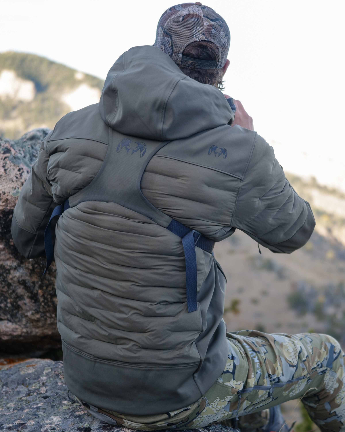 Back of hunter sitting on rock  wearing Axis Thermal Hooded Jacket in Ash Brown