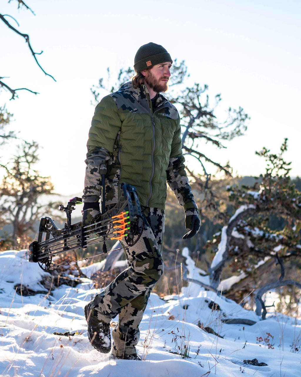 Front, Angled View of Hunter Hiking with Bow in Hand Wearing Axis Thermal Hybrid Hooded Jacket in Verde Camouflage