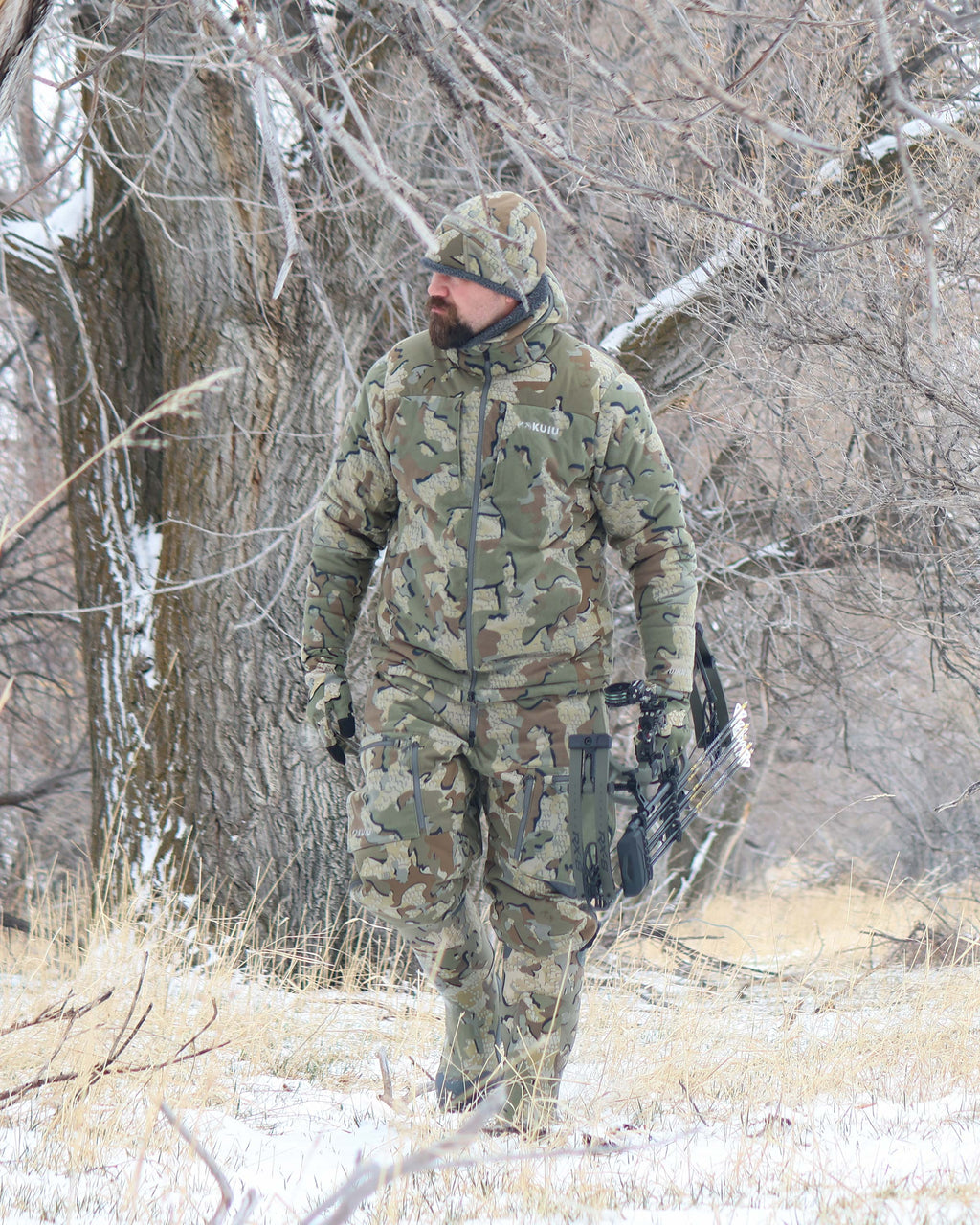 Hunter walking through the woods, wearing Super Down Haven Hooded Jacket in Valo Camouflage