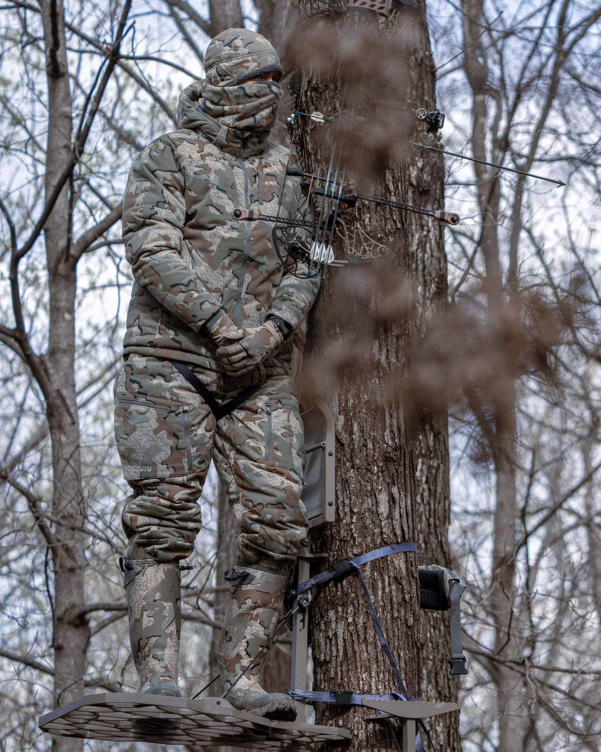 Hunter standing in a tree stand, camouflaged, wearing Super Down Haven Hooded Jacket in Valo Camouflage