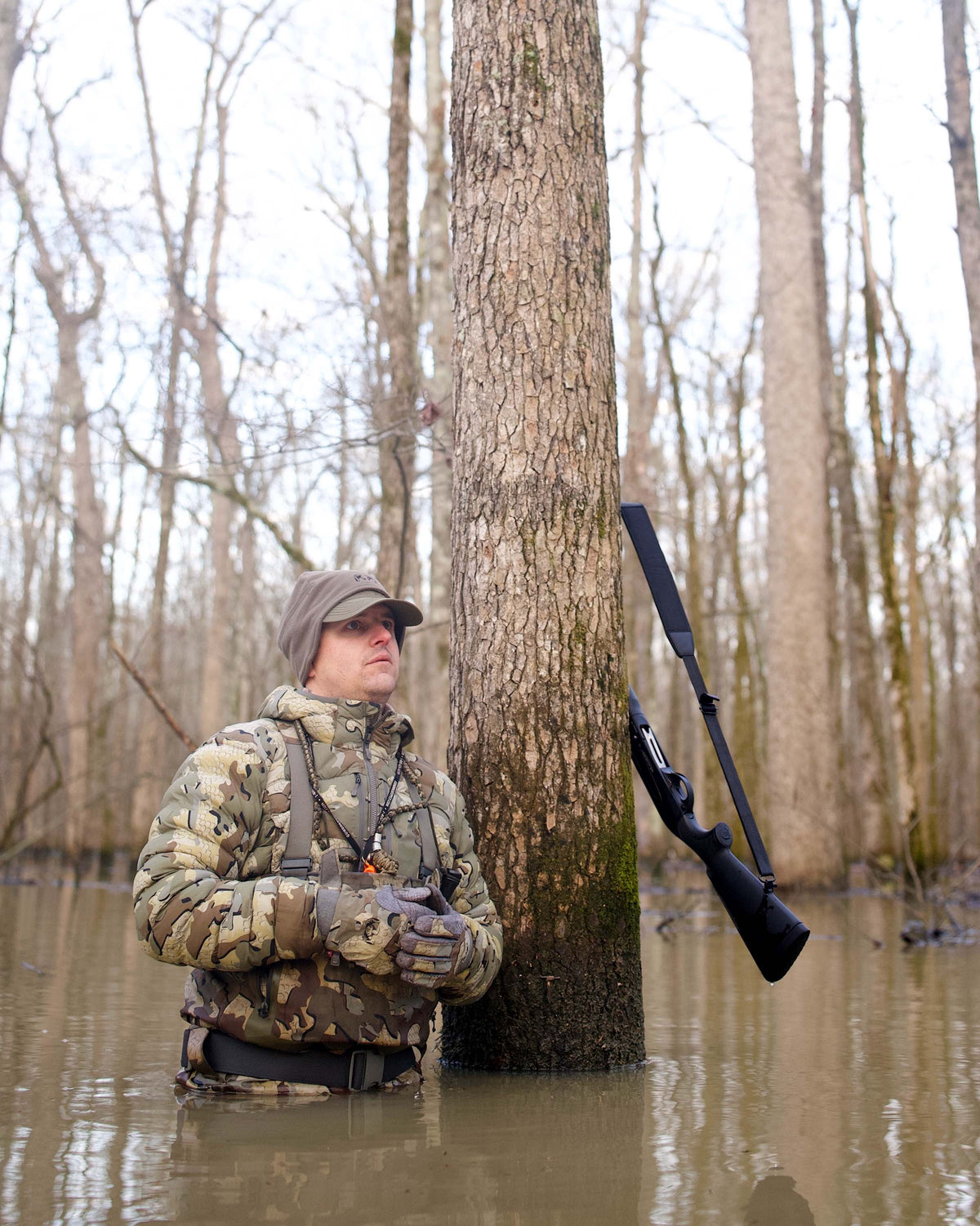 Hunter Wearing Flyway Insulated Hooded Jacket in Valo Camouflage Standing Against a Tree in Flooded Timber