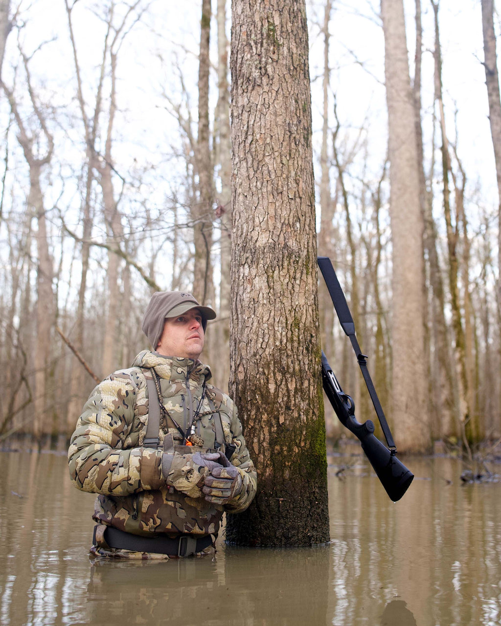 Hunter Wearing Flyway Insulated Hooded Jacket in Valo Camouflage Standing Against a Tree in Flooded Timber