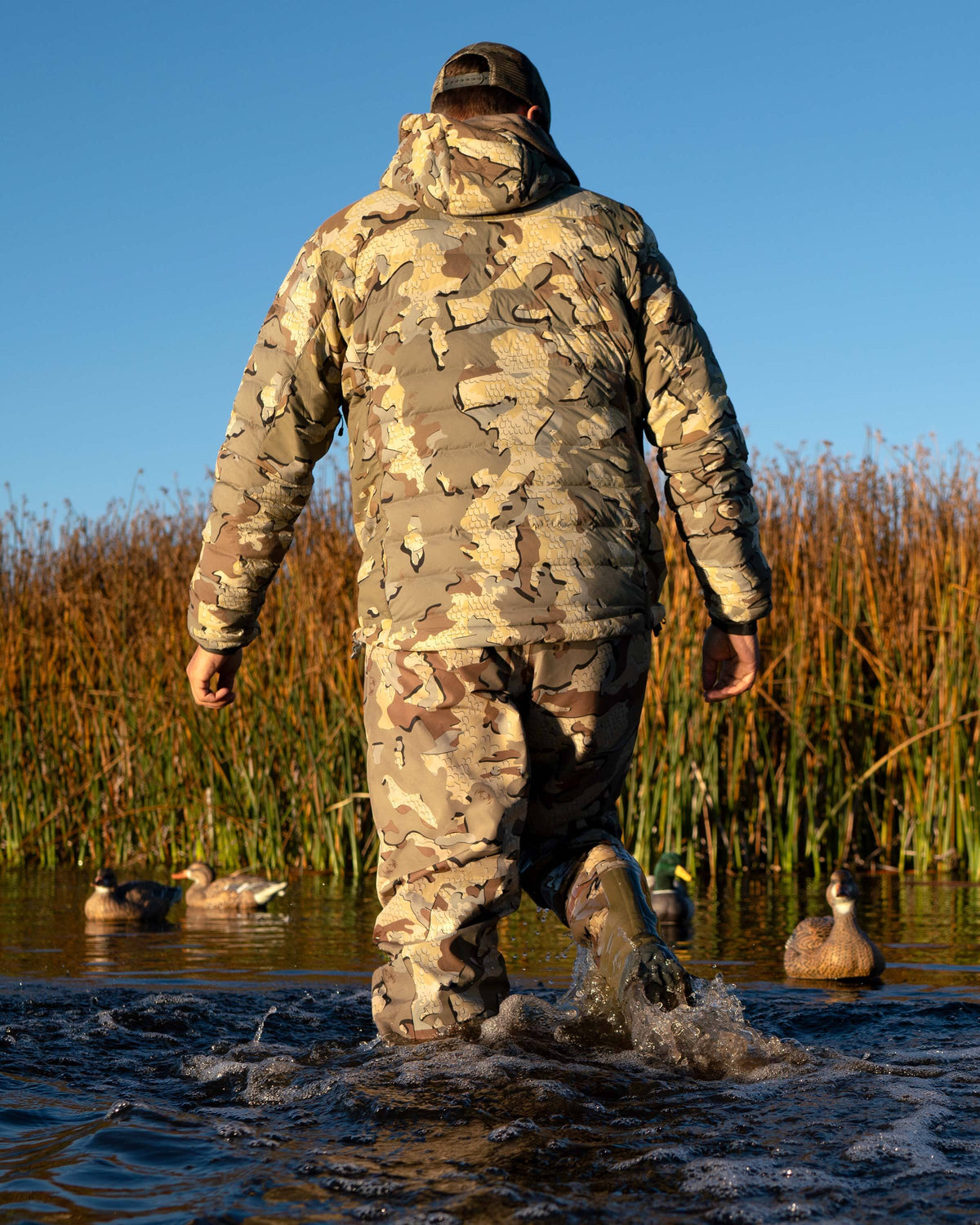 Back of Hunter Wearing Flyway Insulated Hooded Jacket in Valo Camouflage walking towards Tules with Decoys in the Water