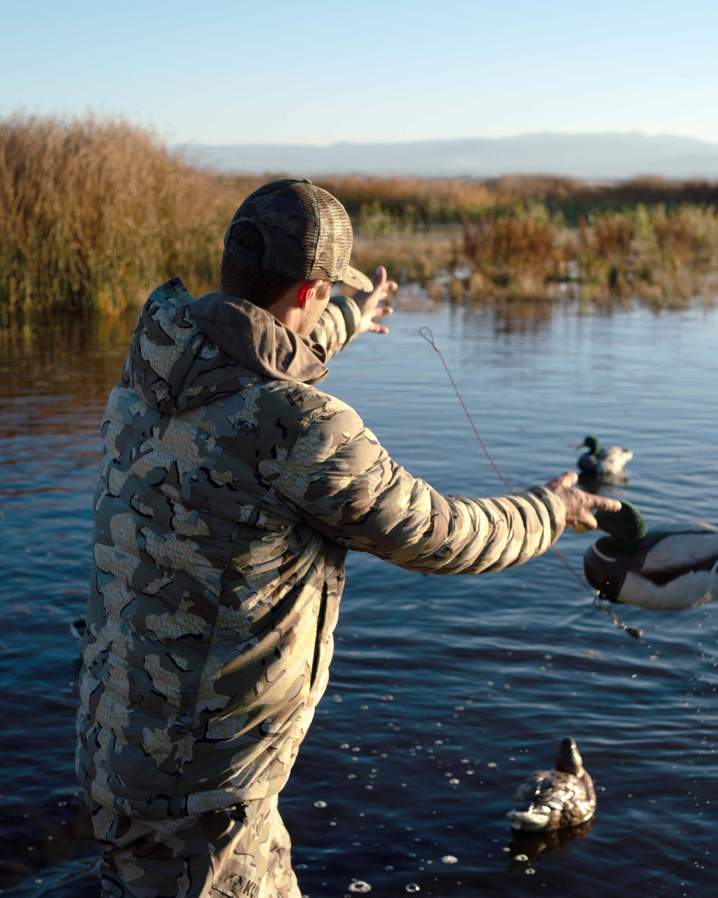 Hunter Wearing Flyway Insulated Hooded Jacket in Valo Camouflage Showing side Zippered Pocket and Hood