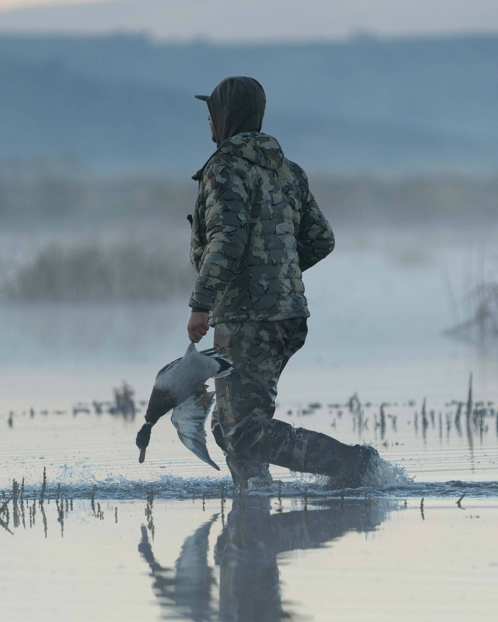 Hunter Wearing Flyway Insulated Hooded Jacket in Valo Camouflage holding a Drake Mallard in the Fog Showing Sektor Insulation Baffles