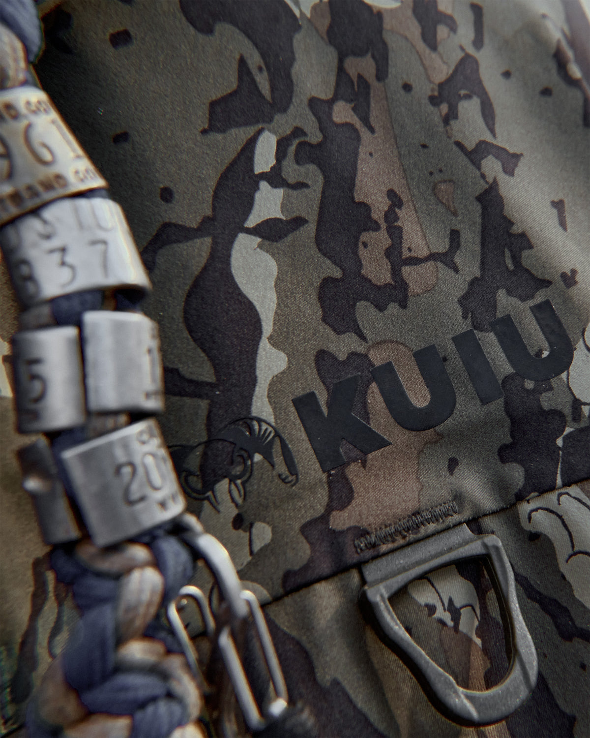 Close-up of KUIU logo on front chest pocket featuring a D-ring and call attachment.
