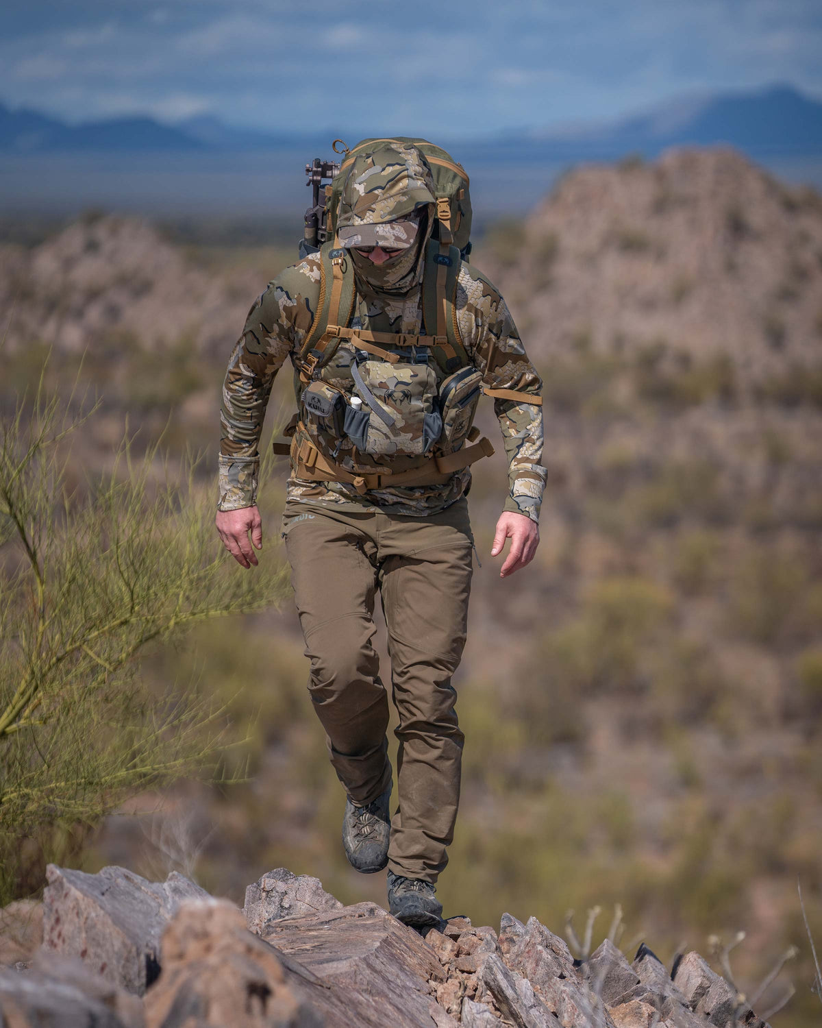 Hunter Walking on Ridge in the Desert Wearing Pro Brush Pants in Bourbon Brown