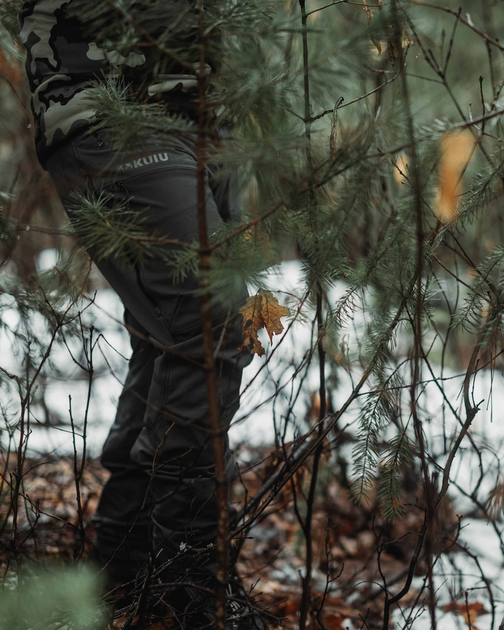 Angled, Front view of Hunter Hiking in Pine Forest Wearing PRO Brush Pant in Gunmetal Grey Color
