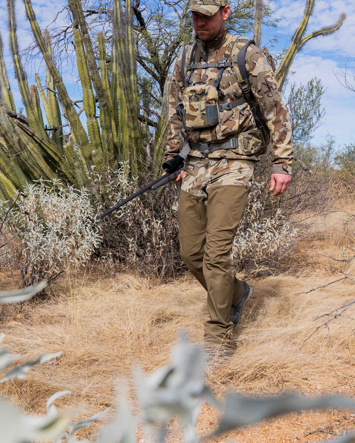 Hunter carrying weapon walking through brush wearing PRO Brush Pant in Valo Camouflage
