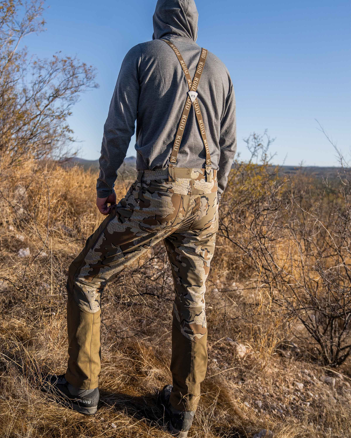 Back of hunter in thorny area wearing PRO Brush Pant in Valo Camouflage showing suspenders in use