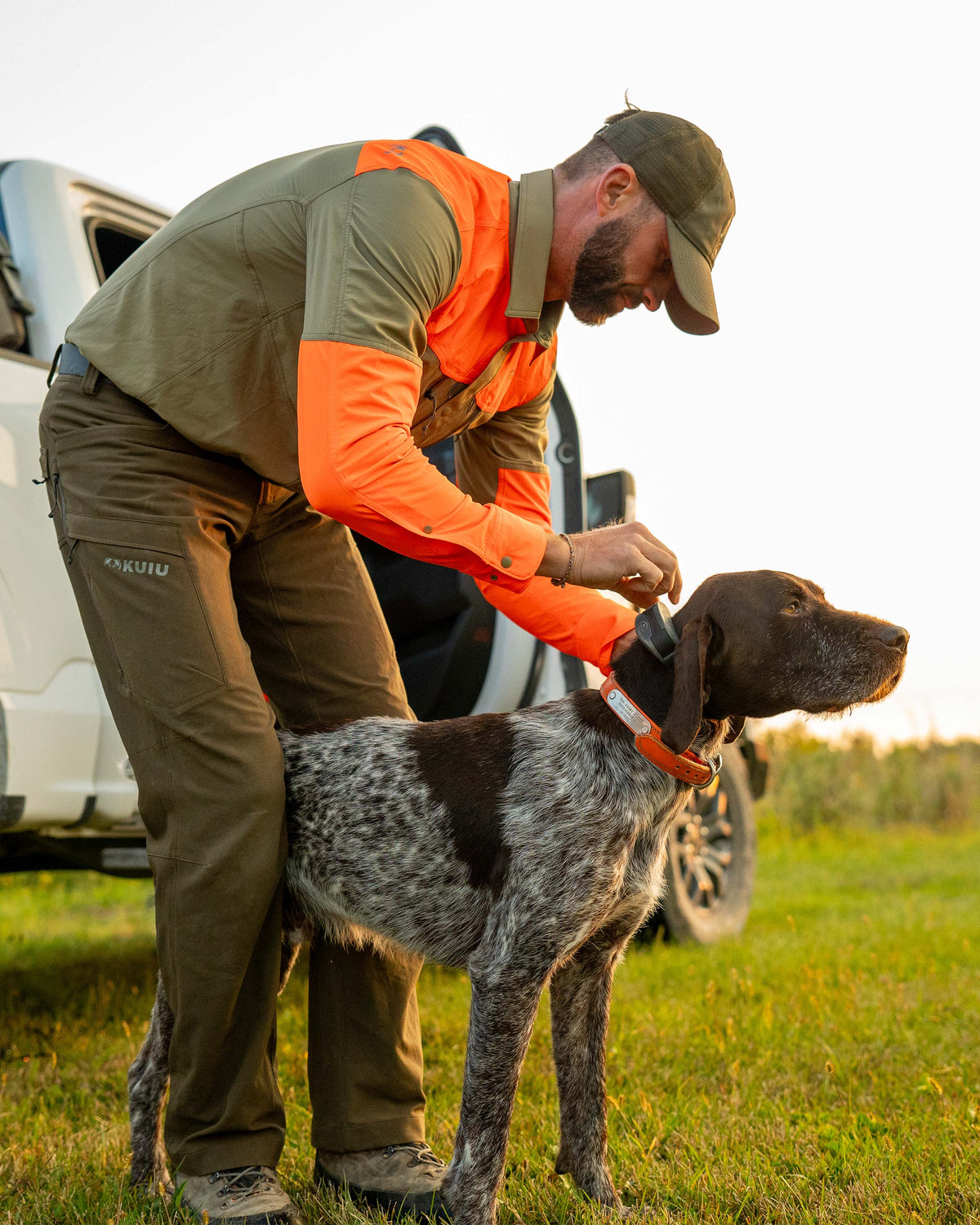 Hunter adjusting dog collar on his dog, wearing Upland Sporter Shirt in Khaki/Blaze Orange