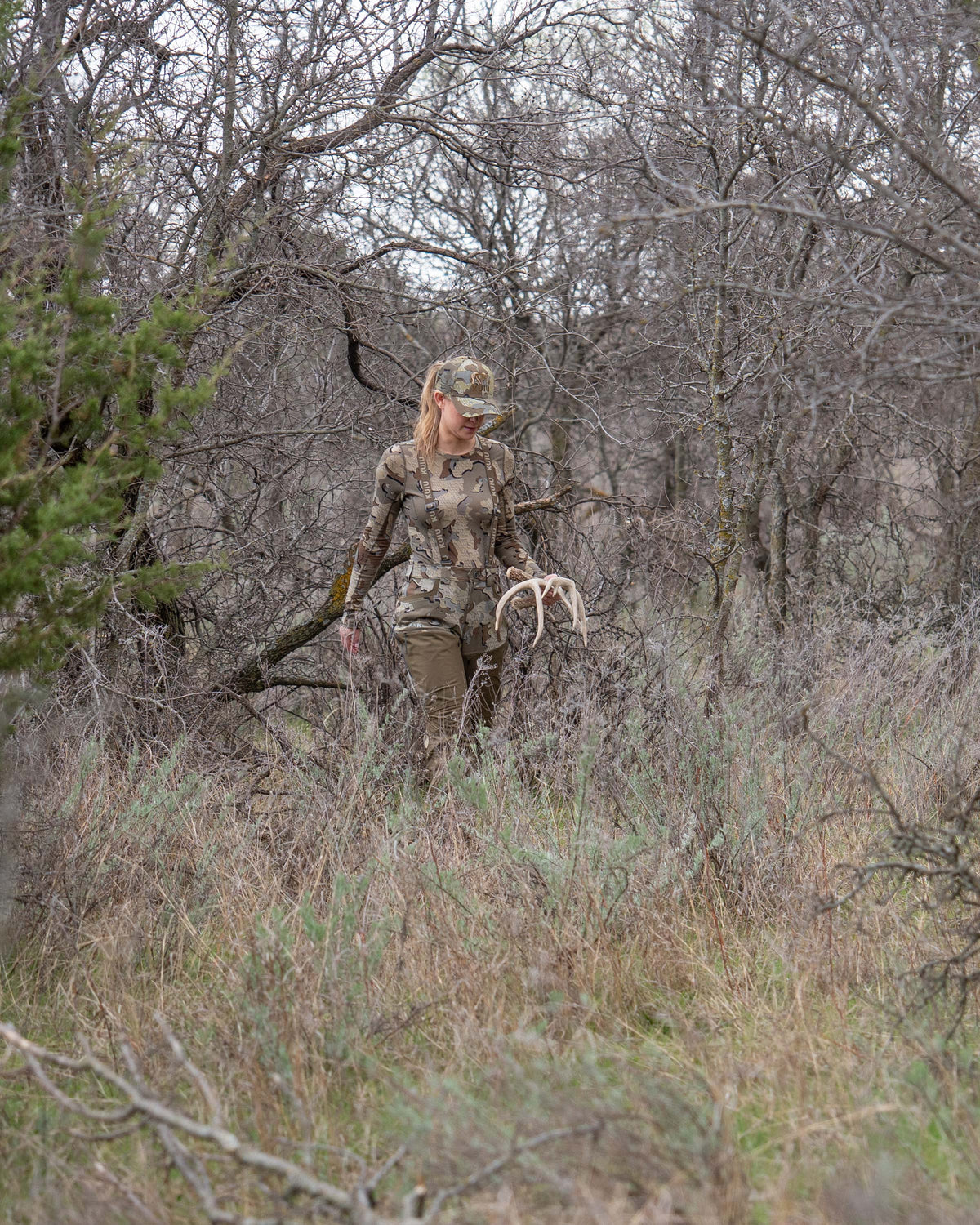 Woman hunter walking through brush terrain with sheds in hand wearing Women's PRO Brush Pant in Valo Camouflage