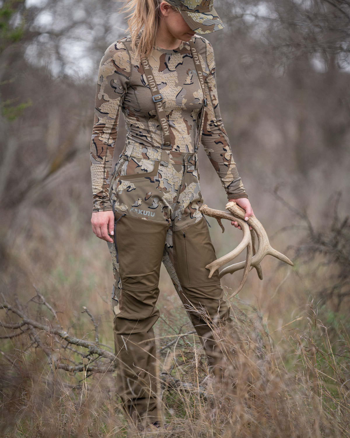 Woman hunter standing in brush terrain with sheds in hand wearing Women's PRO Brush Pant in Valo Camouflage