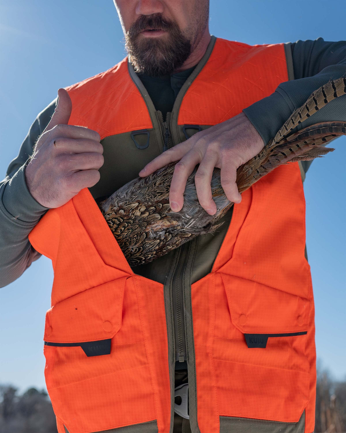 Hunter wearing a Core Upland Vest in Blaze Orange putting a bird in the front pocket.