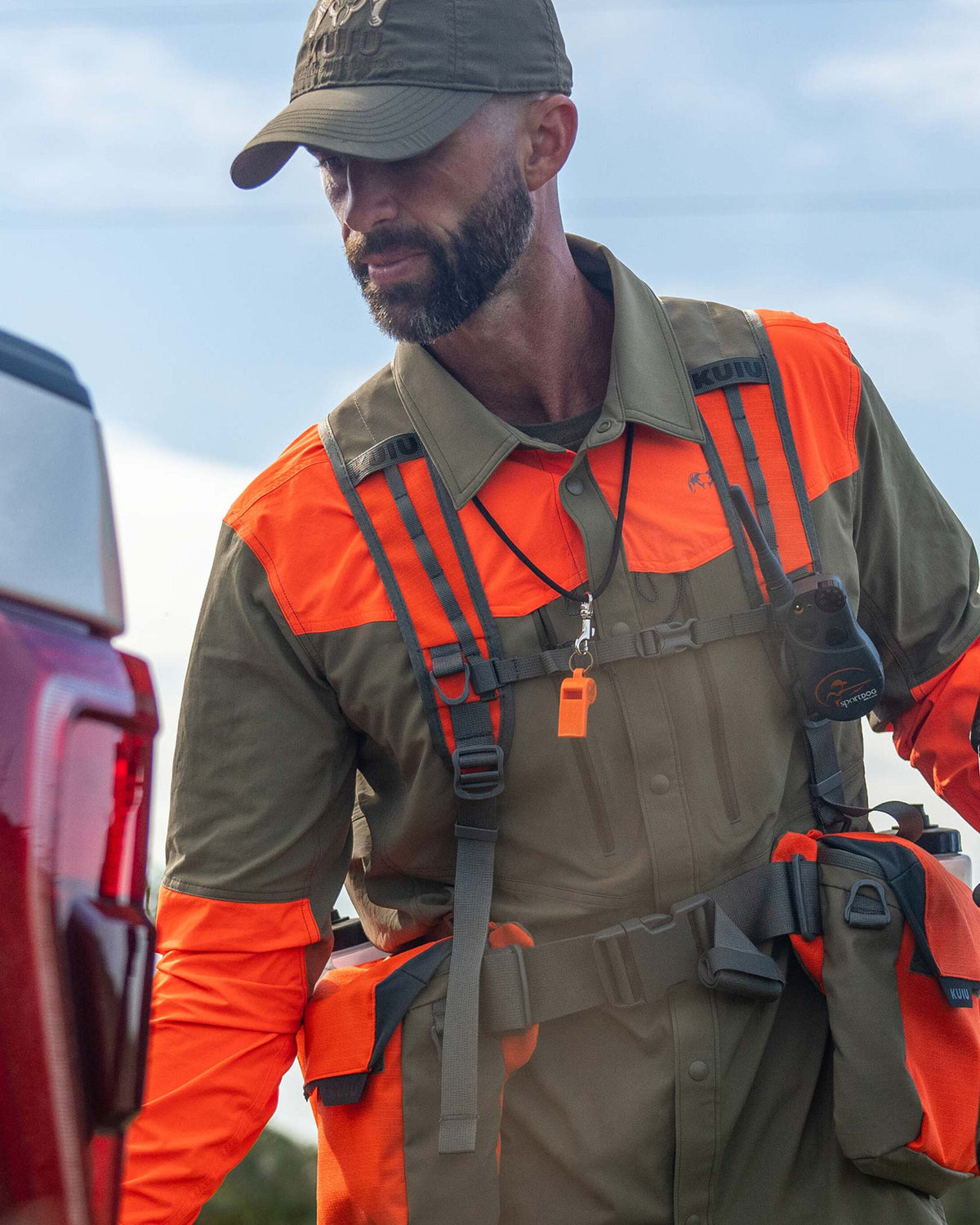 Hunter reaching to close his truck tailgate, wearing Upland Field Vest in Blaze Orange